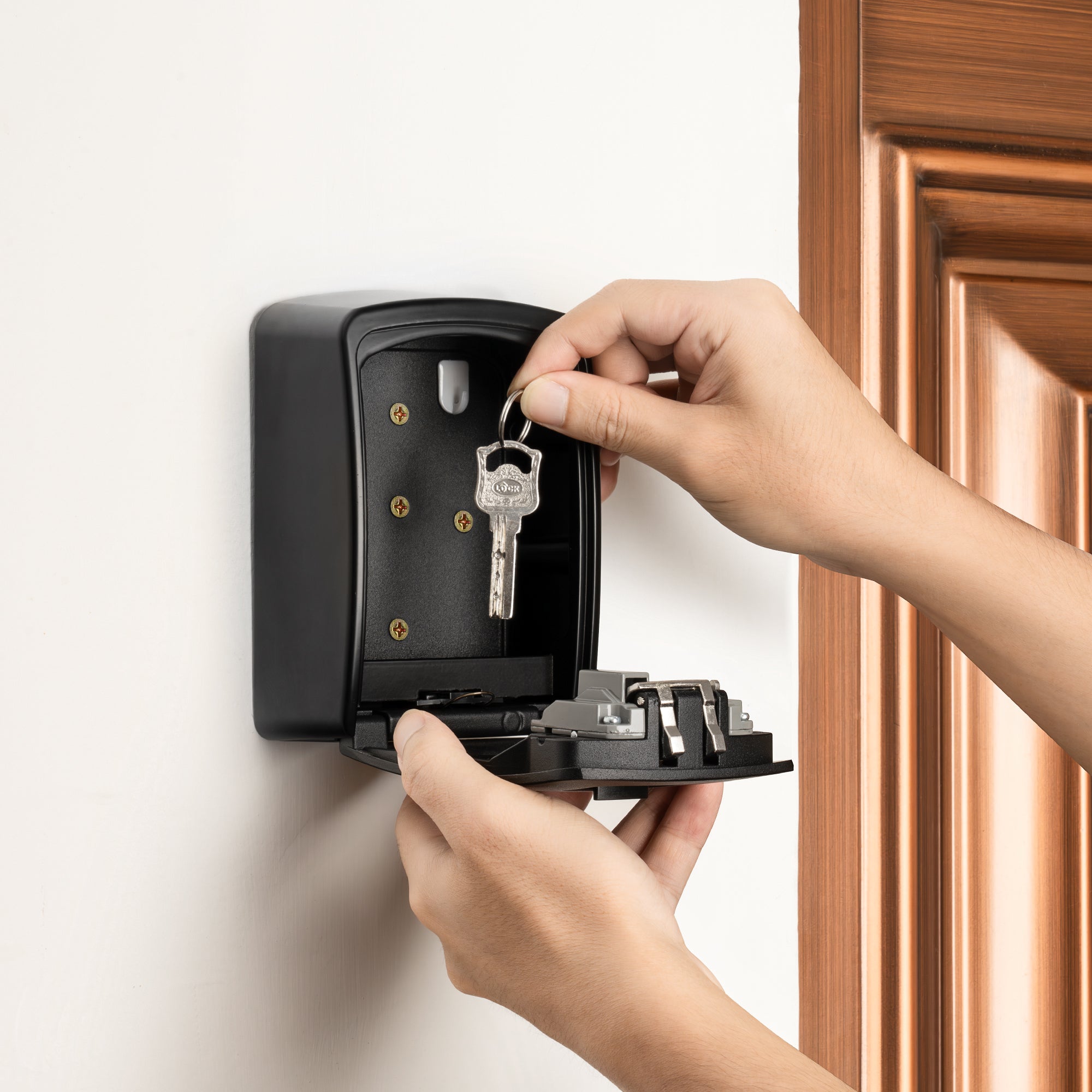 Hand plaatst een sleutel in een Sleutelkluisje Pro XL aan de muur, ideaal voor veilig sleutelbeheer binnen en buiten.